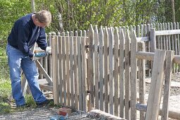 Man builds wooden fence with gate for organic garden