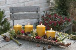 4 yellow candles in bark, decorated with ilex, red berries