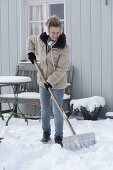 Frau schippt Schnee auf der Terrasse