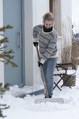 Frau schippt Schnee auf der Terrasse