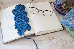 Blue crocheted bookmark and reading glasses on open book