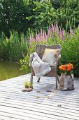 Tasche mit Dahlien neben einem Korbstuhl auf dem Steg am See