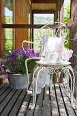 Vintage-style crockery on ornate metal table and chair on wooden deck