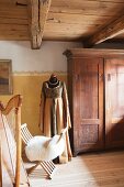 Historical clothing on tailors' dummy next to antique wooden wardrobe, sheepskin on chair and harp
