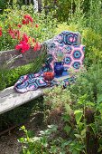 Crocheted blanket and cushions on wooden bench in cottage garden
