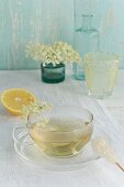 Elderflower tea in a cup, elderflowers, lemon and a rock candy stick