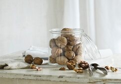 Walnuts in and next to a glass jar with a nutcracker on a rustic kitchen table