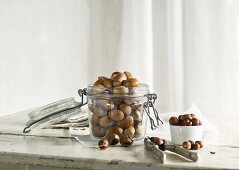 Hazelnuts in and next to a glass jar and a nutcracker on a rustic kitchen table