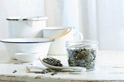 Pumpkin seeds in a glass jar and on a spoon on a rustic kitchen table