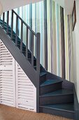 Striped wallpaper in stairwell with storage cupboards below wooden staircase