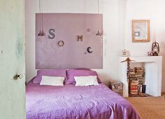 Double bed with purple bed linen, colour coordinated panel on wall and disused fireplace