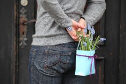 Person holding bag of grape hyacinths behind back
