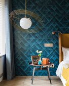 Schlafzimmer mit Retro Pendelleuchte und petrolfarbener Textiltapete mit geometrischem Muster