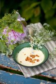 Bowl of vanilla pudding with brittle topping next to peonies, lady's mantel and chervil