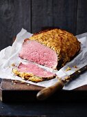 A joint of roast beef with an onion crust and one slice cut off