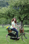 Junge Frau auf Fahrrad, Fahrradkorb mit Sonnenblumen gefüllt