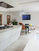 Moderne weiße Wohnküche mit Kochinsel und Esstisch