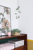 Leaves and fir sprigs in glass baubles hung above retro sideboard