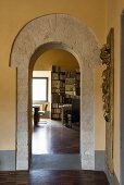 View of parquet floor and bookcase in living area seen through stone archway