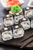 Sushi-Rollen mit schwarzen Sesamsamen, Aal und Frischkäse auf einem Holzbrett