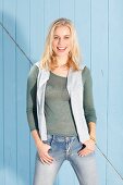 A blonde woman wearing a green knitted top, a grey pullover draped around her shoulders and jeans