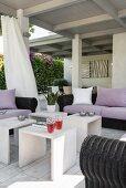 Comfortable black rattan sofas with mauve cushions and scatter cushions and several sire tables on roofed terrace