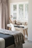 Desk below window with slatted shutters in bedroom