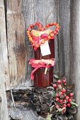 Stacked jars of jam decorated with rose-hip love-heart against rustic board wall