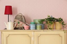 Houseplant, tins and table lamp on top of pastel yellow cabinet