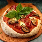 Ganze Vollkorn Pizza mit Schinken, Pilzen, Mozzarella und Basilikum auf Pizzaschieber