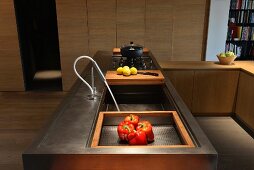 Modern, metal counter with integrated wooden chopping board and gas hob in front of simple fitted cupboards