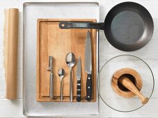 Various kitchen utensils: pan, mortar, peeler, knives, spoons, baking paper