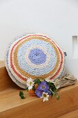Flowers next to round cushion with crocheted cover made from T-shirt yarn