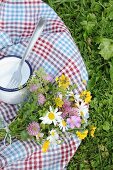 Karierte Picknickdecke mit buntem Wiesenblumenstrauß und Emailletasse im Gras