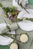 Dekorierte Kerzen und buntem Wiesenblumenstrauß auf grün-weiss karierter Tischdecke