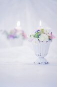 Romantisches Blumengesteck mit brennender Kerze vor Spiegel
