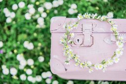 Wreath of daisies on pink suitcase on lawn