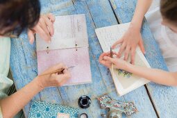 Two people sitting at wooden table and writing in poetry album