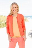 A blonde woman on the beach wearing a T-shirt, cardigan and trousers in different orange tones