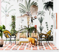Dining table with light chairs in front of jungle-themed wallpaper