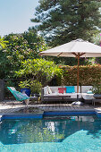 Outdoor sofa under the parasol by the pool in the garden
