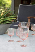 Pink relief glasses and water carafe on marble table