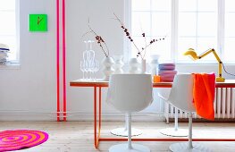 Neon-Ambiente mit filigranem Metall-Tischgestell, pinkfarben lackierten Rohrleitungen und neongrüner Wanduhr