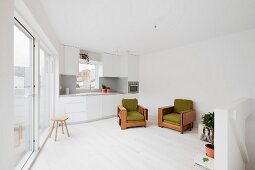 weiße Einbauküche in Dachgeschoss mit Terrassentür, weißem Dielenboden und grün gepolsterten Vintage Sesseln