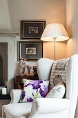 Floral scatter cushion on wing-back chair in front of standard lamp in corner