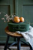 Kleiner Vintage Koffer mit Zinnteller und Eiern auf Hocker