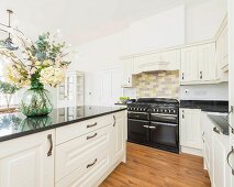 Naturweisse Landhausküche mit Küchentheke, Granitarbeitsplatte und schwarzem Gasherd