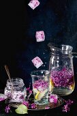 Fliederblüteneiswürfel fallen in Glas mit Fliederblütenlimonade