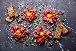 Beef tartare with pickled cucumber and fresh onion on dark marble background