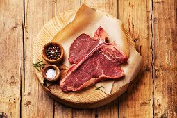 Raw fresh meat T-Bone Steak with salt and pepper on cutting board on wooden background